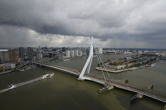 Bird's eye view of Erasmus bridge and skyline of Rotterdam in the Netherlands. A cruise ship passes under the bridge and storm clouds are overhead; Rotterdam, Netherlands