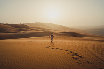 Fototapeta na wymiar Woman running towards the sun at the moreeb dunes in Rub Al Khali in the UAE