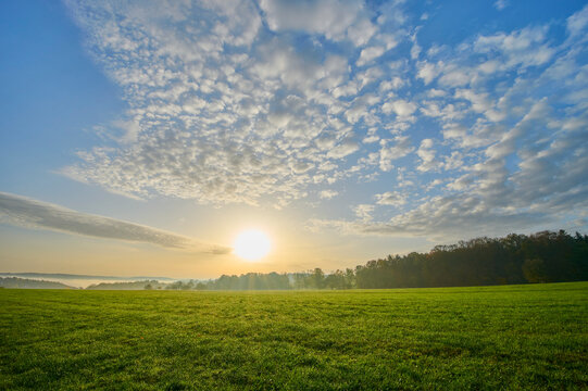 Sunrise over meadow with puffy altocumulus clouds in a blue sky in Vielbrunn; Michelstadt, Hesse, Germany