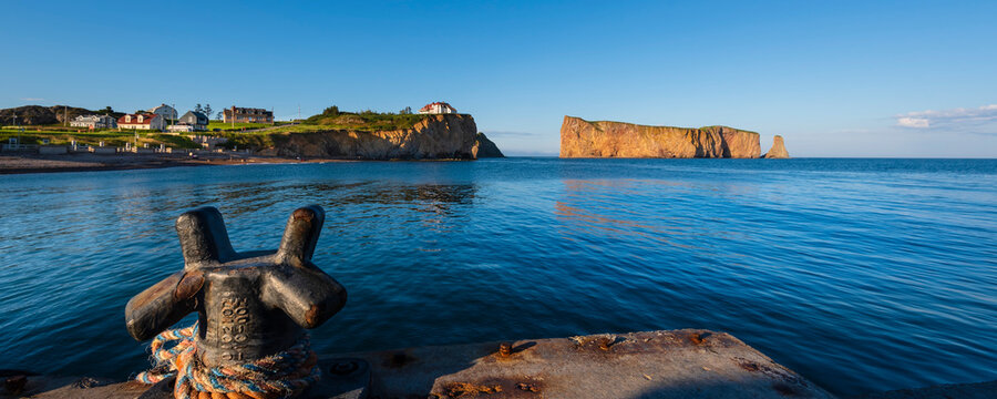 Panoramic view of Perce Rock and house on cliff edge with bright blue sky; Quebec, Canada