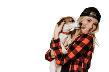 Adorable blonde in baseball cap and checked shirt , broad smiling, hugs her puppy Jack Russel, who is licks her cheek, over transparent background. Pets and hosts. Happiness concept.