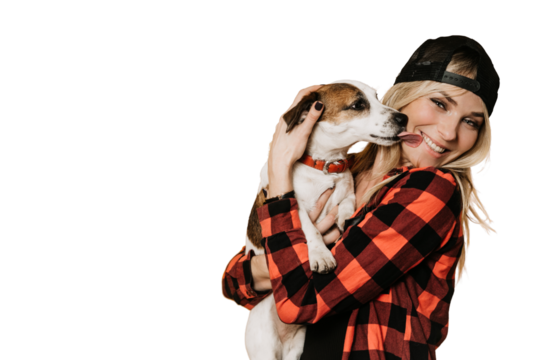 Adorable blonde in baseball cap and checked shirt , broad smiling, hugs her puppy Jack Russel, who is licks her cheek, over transparent background. Pets and hosts. Happiness concept.