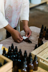 Hands of an unrecognizable person placing labels on glass bottles with oils.