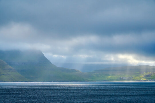 View from the island ferry Norrona when approaching the Faroe Islands, with sunlight streaming through the clouds to the water and land below; Faroe Islands, Denmark