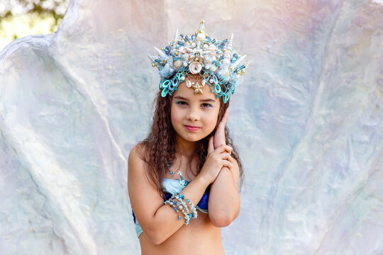 A beautiful little girl in a crown and mermaid costume in a large seashell
