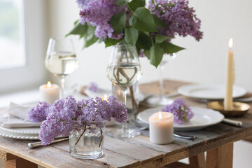 Beautiful table decor for a wedding dinner with a spring blooming lilac flowers. Celebration of a special event. Fancy white plates, wineglasses, candles. Countryside style