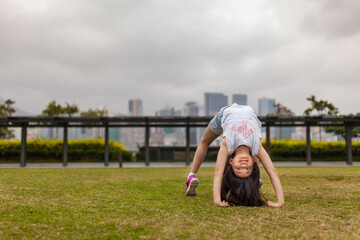 Young girl doing gymnastics in a park with the skyline of Hong Kong in the background; Hong Kong, China