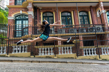 Girl leaping in mid-air in front of a building in a public park; Hong Kong, China