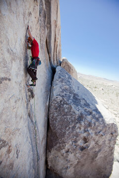 A trad climber ascends a shallow crack on a vertical granite wall.