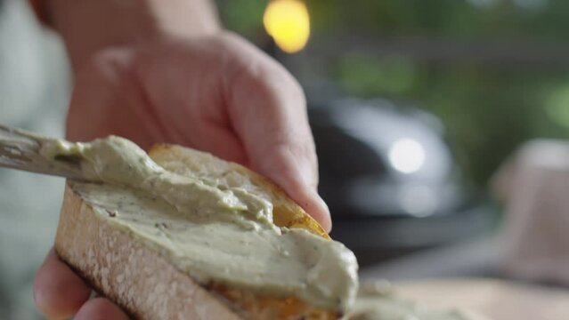 Close up selective focus shot of hands of man spreading topping on slice of toasted ciabatta bread
