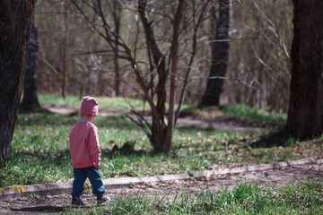 A three-year-old child walks in the park in the spring, on a sunny day.