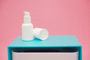Serum bottle with water drops on blue cupboard and pink degraded background
