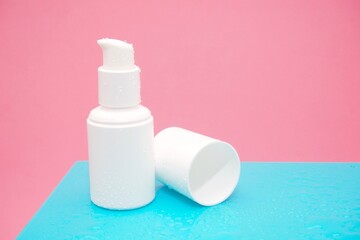 Serum bottle with water drops on blue cupboard and pink degraded background