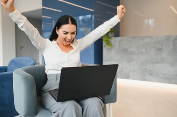 Portrait of excited young caucasian woman celebrating success while sitting with laptop at home or...