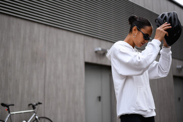 Young african american woman in sunglasses wearing safety helmet near blurred bike on street 
