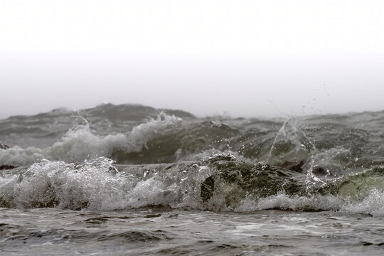 Close-up detail of an approaching wave breaking at the shore with a white overcast sky; South Shields, Tyne and Wear, England