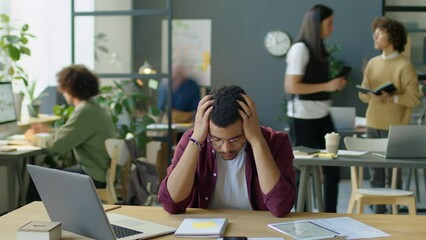 Time lapse of young businessman sitting at office workplace with head in hands while suffering from stress or headache during day
