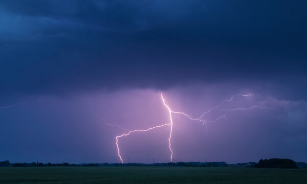 A lightning bolt arcs out of the base of a dark storm cloud and strikes the ground; Lincolnshire, England