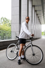 Fit and stylish african american woman standing near bicycle on road 