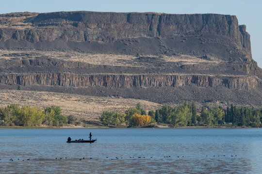 A bass angler fishes in The Devils Punchbowl on Banks Lake below the towering north end of Steamboat Rock, Steamboat Rock State Park; Grand Coulee, Washington, United States of America