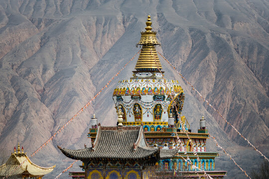 The rooftop of a Buddhist Temple at the Labrang Monastery with the mountain ridges of the Himalayas in the background; Labrang, Amdo, Tibet