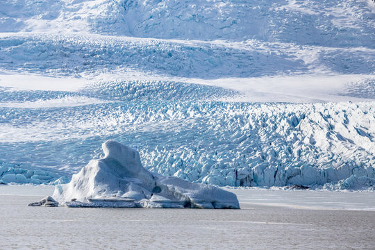 un iceberg emerge dalla laguna ghiacciata, sullo sfondo la lingua del ghiacciaio Fjalls&aacute;rl&oacute;n con i crepacci ben visibili