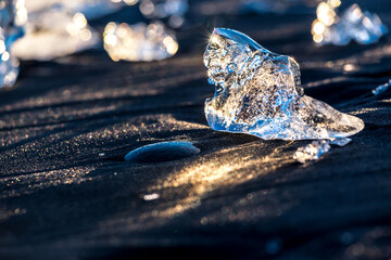 Piccolo blocco di ghiaccio che brilla posato su spiaggia nera illuminato da raggi di sole al tramonto 