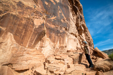 Female tourist admires ancient petroglyphs depicting lizards on a rock face in Dinosaur National Monument; Utah, United States of America