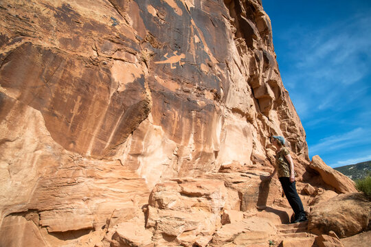 Female tourist admires ancient petroglyphs depicting lizards on a rock face in Dinosaur National Monument; Utah, United States of America