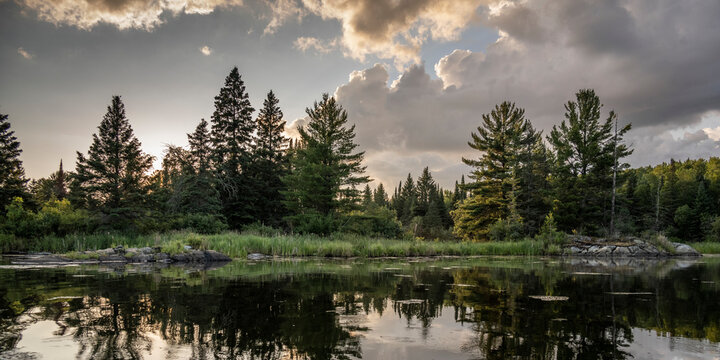 Sunset light warms a scenic landscape and it's mirror image is reflected on water, Lake of the Woods, Ontario; Kenora, Ontario, Canada