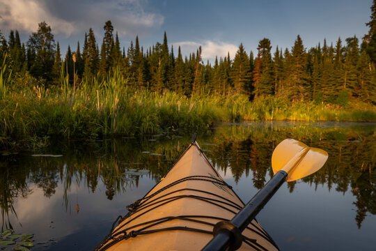 Kayaking along the shoreline of a beautiful lake with the bow of a yellow kayak and paddle visible, Lake of the Woods, Ontario; Kenora, Ontario, Canada