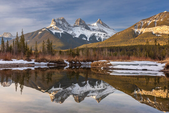 Three Sisters snow-capped mountain peaks reflected in a mirror image in a lake in Alberta, Canada; Canmore, Alberta, Canada