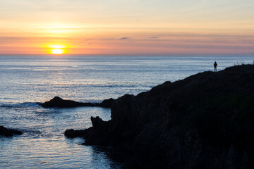 Dramatic California sunset off the coast in Mendocino, California with sun in horizon and person on a distant cliff looking to the sea.