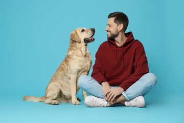 Happy man with his cute Labrador Retriever on turquoise background
