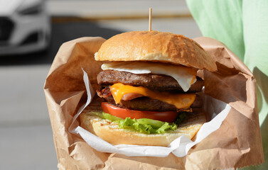 Woman holding delicious burger in paper wrap on city street, closeup