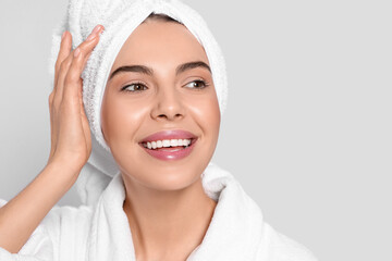 Young woman in bathrobe with towel on light grey background, space for text. Spa treatment