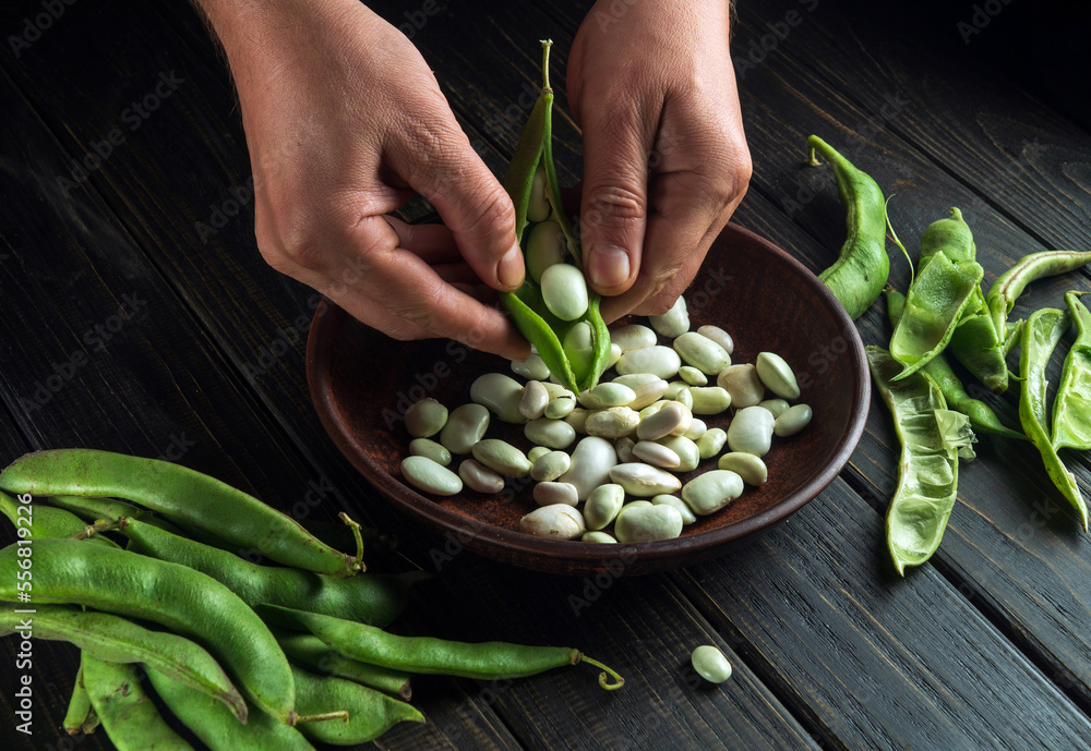 Wall mural Chef in the kitchen cleans the beans from the green pods. Peasant food. Organic vegetables after harvest