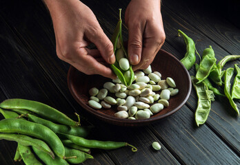 Chef in the kitchen cleans the beans from the green pods. Peasant food. Organic vegetables after...