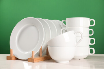 Set of clean dishware on white table against green background