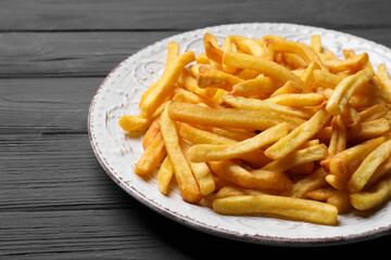 Plate of tasty french fries on black wooden table, closeup