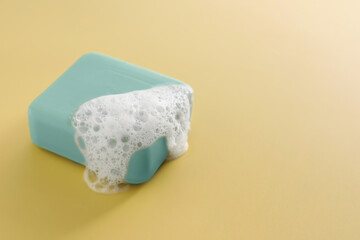 Soap bar with fluffy foam on yellow background, space for text
