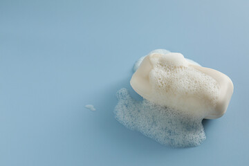 Obraz na płótnie Canvas Soap bar with fluffy foam on light blue background, space for text