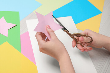 Woman cutting paper star with scissors at white wooden table, closeup