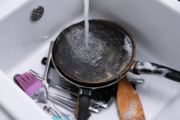 Pouring water on dirty kitchenware and cutlery in sink
