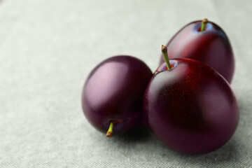 Tasty ripe plums on light fabric, closeup. Space for text