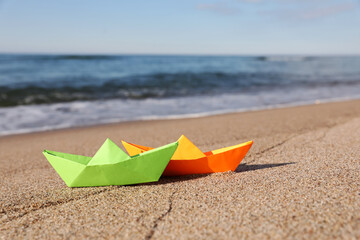 Bright color paper boats on sandy beach near sea