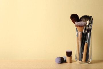 Set of professional makeup brushes on wooden table against beige background, space for text