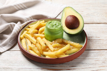 Plate with french fries, guacamole dip and avocado served on white wooden table