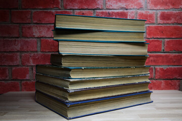 Eight old hardcover books stacked on top of each other on a wooden table.