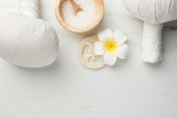 Flat lay composition with spa bags, sea salt and plumeria flower on white marble table. Space for text